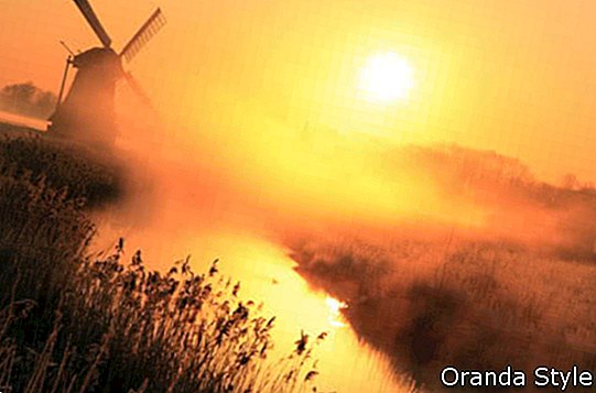 holandiešu saullēkts ar tradicionālajām vējdzirnavām un kanālu