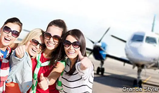 Sonrientes adolescentes o mujeres jóvenes mostrando los pulgares para arriba en el aeropuerto