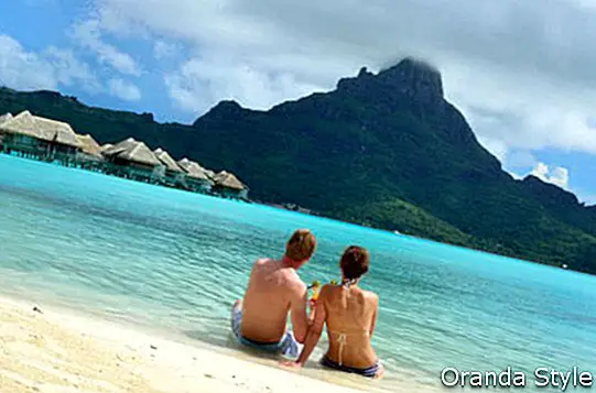 熱帯のボラボラ島を望むラグーンの高級バケーションリゾートのビーチでカクテルを飲む新婚旅行のカップル